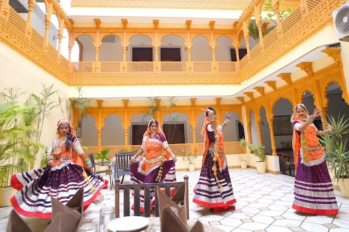 Beautiful traditional Rajasthani courtyard at The Lavitra, Udaipur, featuring ornate yellow sandstone-style arches, intricately carved balconies, indoor plants and a cultural folk dance performance.