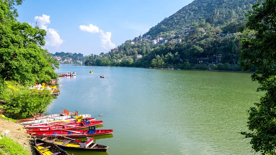 Scenic view of Bhimtal Lake surrounded by green Kumaon hills, with colourful boats on the calm water in Uttarakhand.